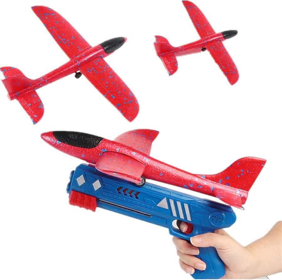 A person's hand holding a blue toy gun with a red foam airplane attached. The airplane has wings and a propeller. The background shows two other red foam airplanes flying.